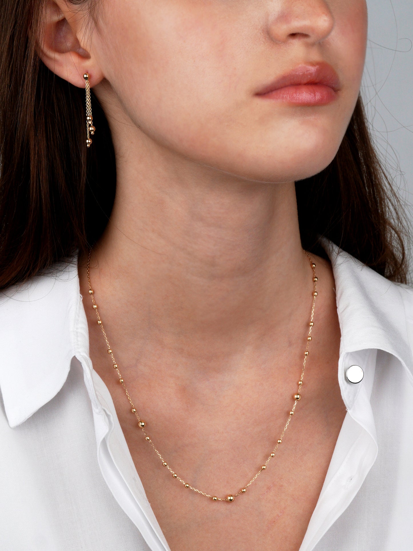 Close-up of a person wearing a gold necklace and earrings-polished gold beads along a delicate chain