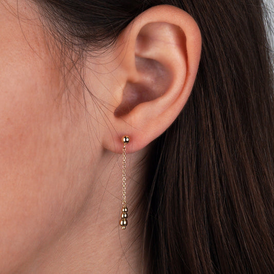 Close-up of an ear wearing a gold earring with dangling beads-Earring size: 27 mm-Simple Everyday Gold Earrings