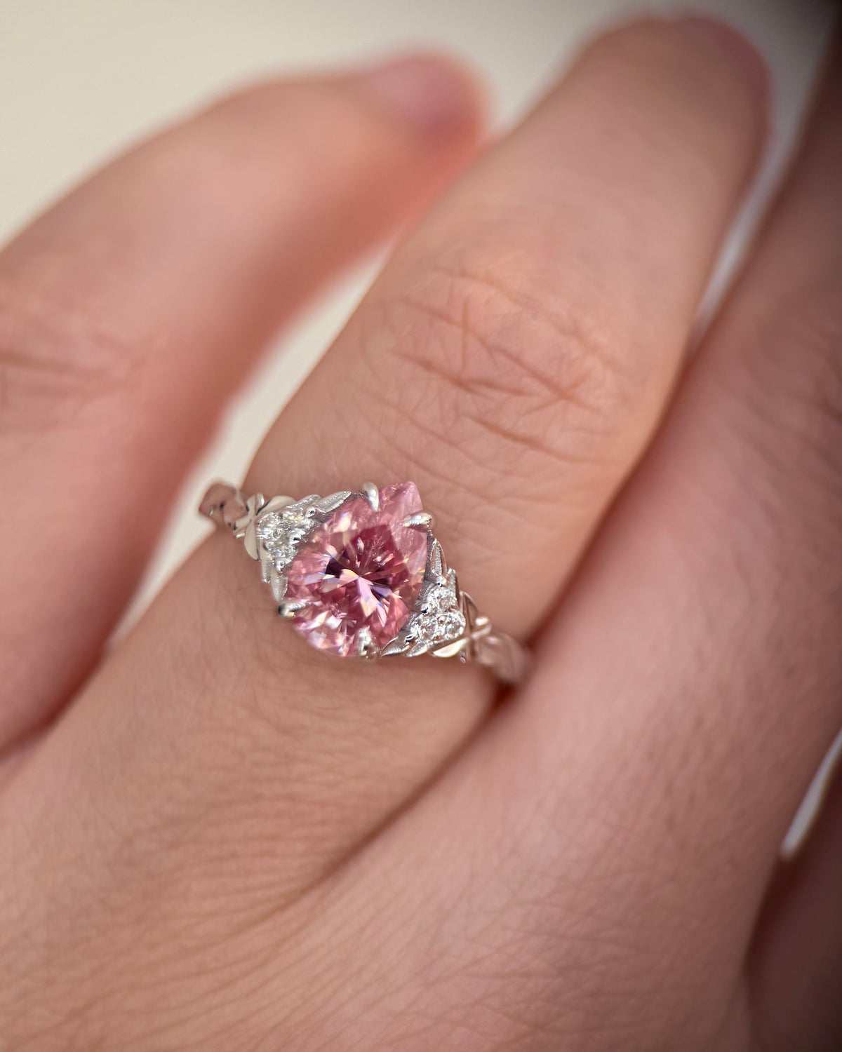 A close-up of a hand wearing a silver ring with a large pink marquise-cut center stone and small clear accent stones on the shoulders-moissanite engagement ring-colored stone ring-unique engagement ring