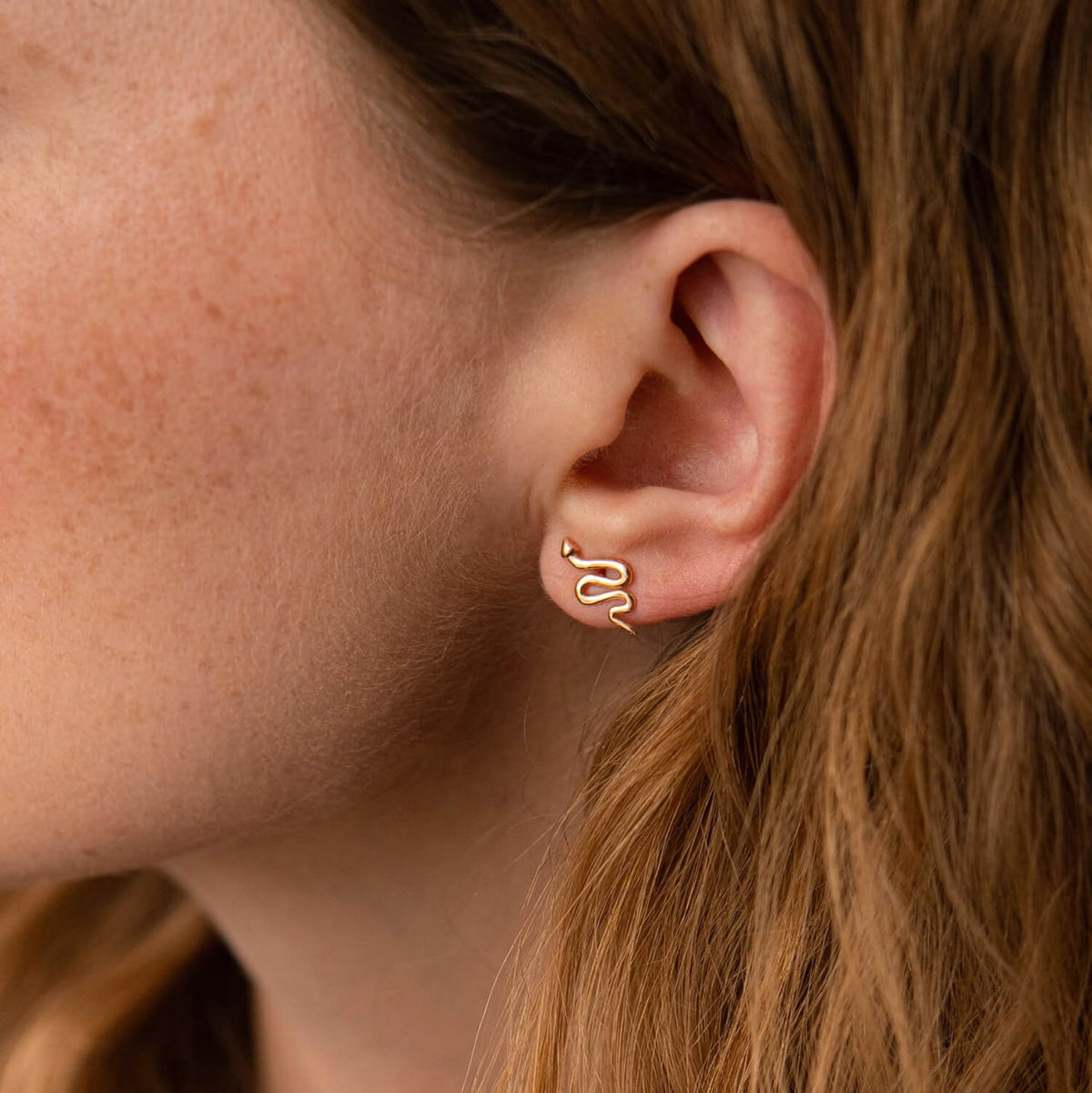 A close-up of a person's ear wearing a delicate gold snake-shaped stud earring-no stone earrings
small gold studs
unique stud earrings