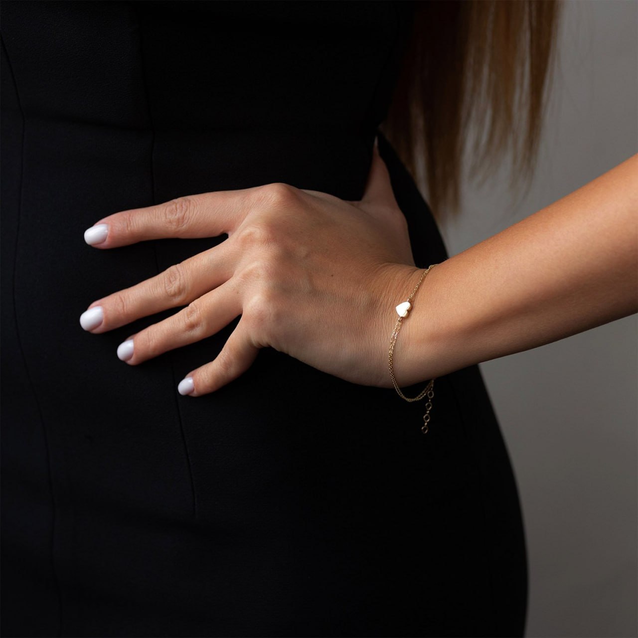 A close-up of a woman's hand and wrist wearing a delicate gold chain bracelet with a small white heart charm-delicate heart jewelry-dainty gold bracelet-layered chain bracelet