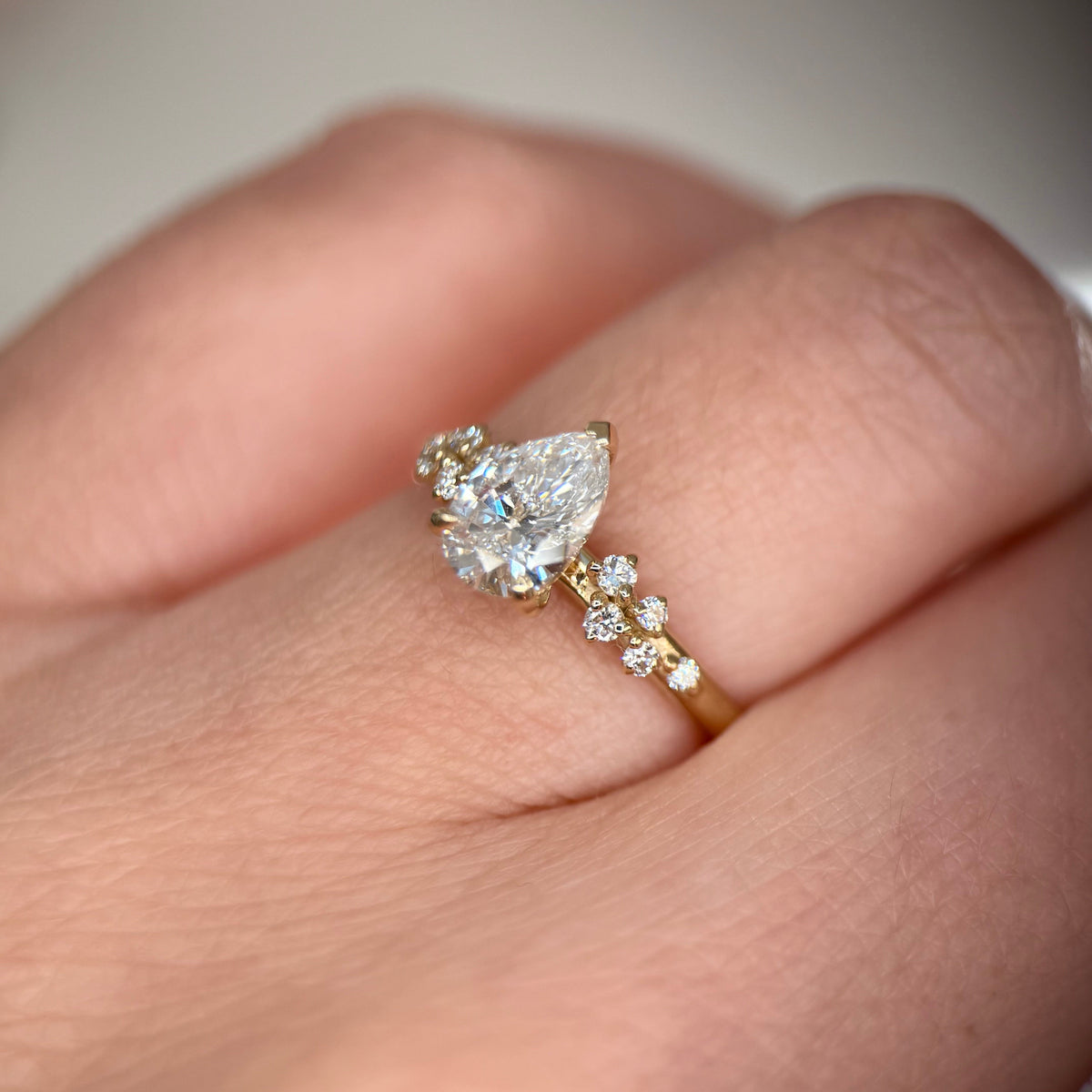 A close-up of a hand wearing a yellow gold ring featuring a pear-cut clear center stone and smaller round stones along the band-Metal: 14k Yellow Gold (585), solid