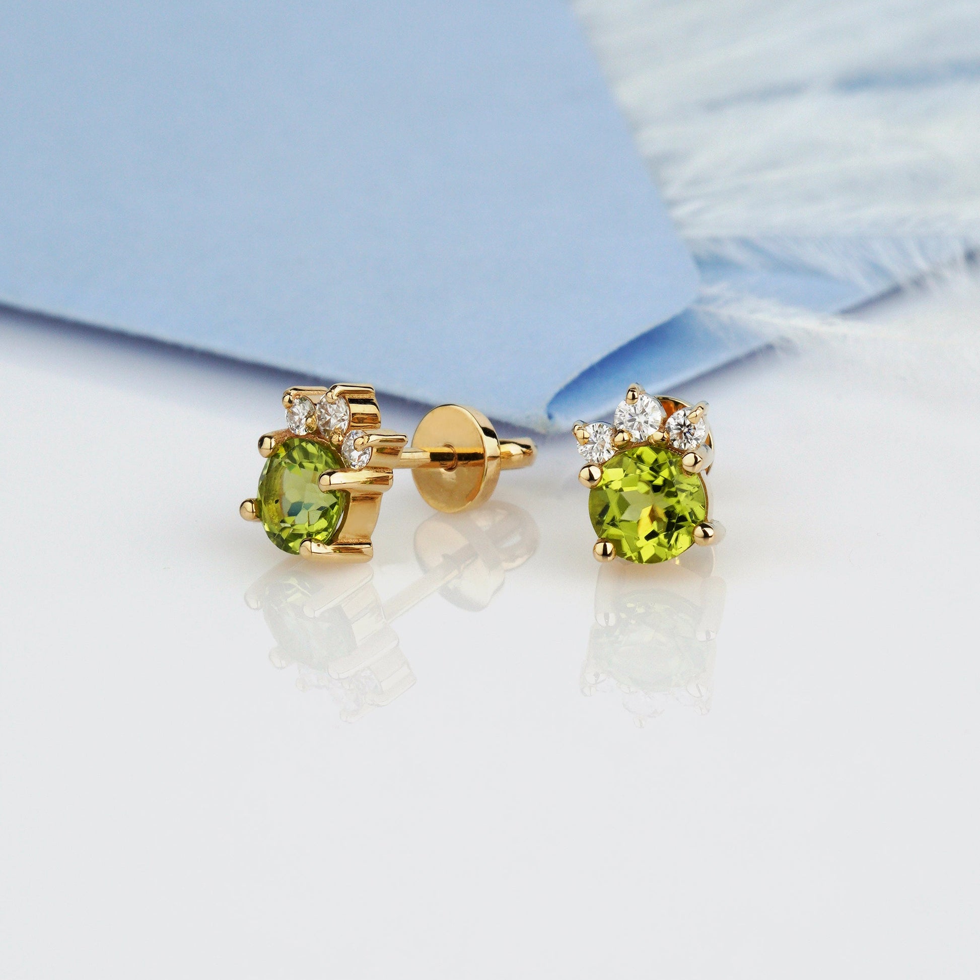 A pair of gold stud earrings with oval green gemstones and small clear stones at the top-gold flower earrings-peridot earrings- moissanite earrings- yellow gold earrings