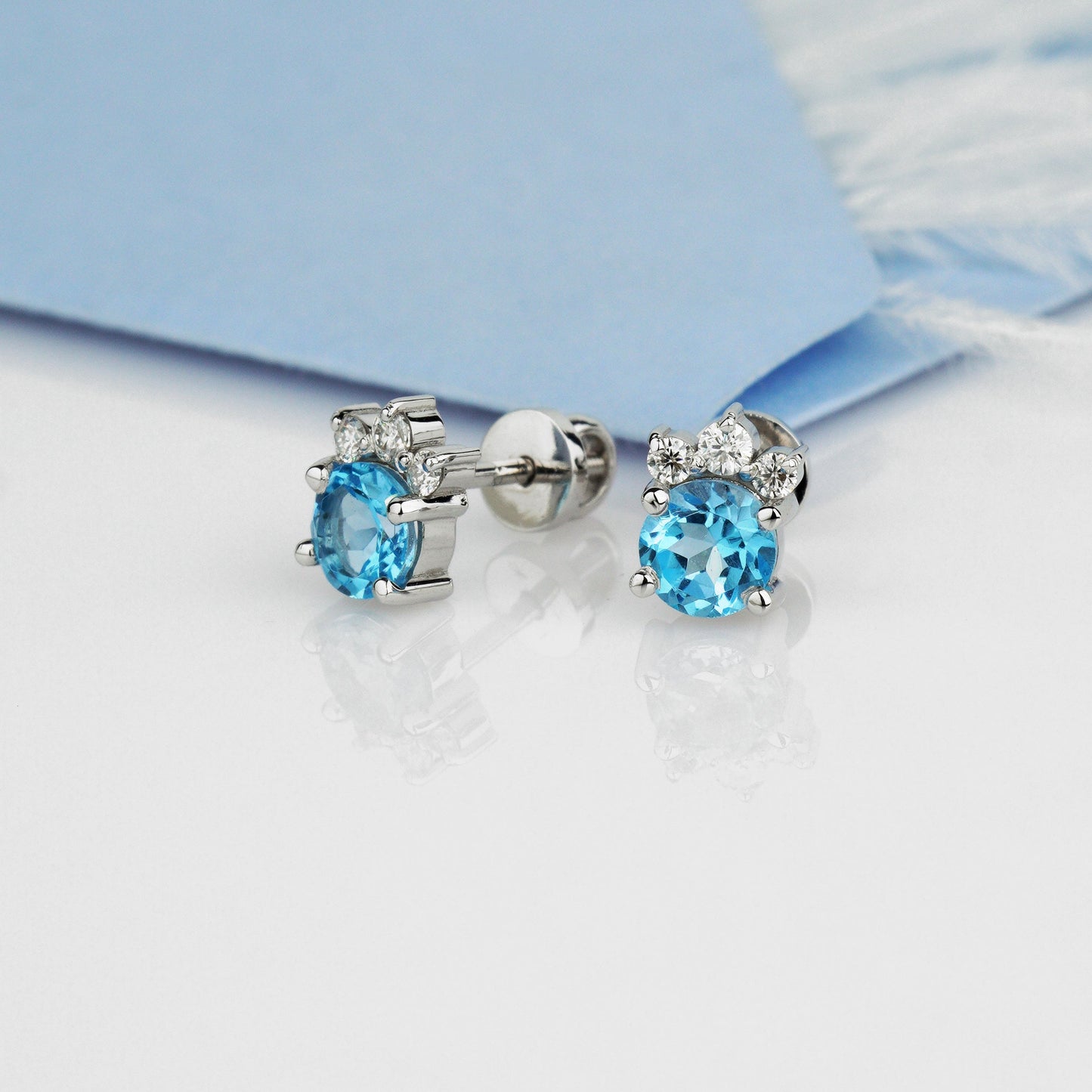 A pair of oval stud earrings with light blue gemstones and small clear accent stones in a silver setting-14k solid gold, 585 fineness-Stones: Swiss Blue Topaz + Moissanites (0.15 ct)-Closure: stud (screw-back)
