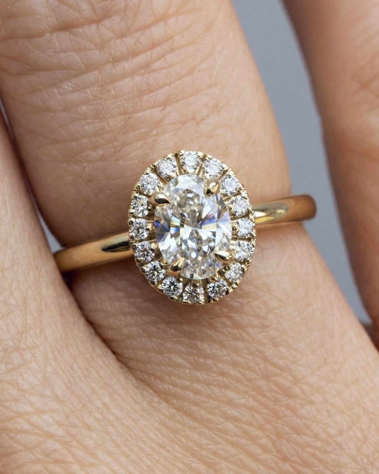  luminous oval diamond engagement ring wrapped in a soft halo of pavé diamonds-halo engagement ring on hand