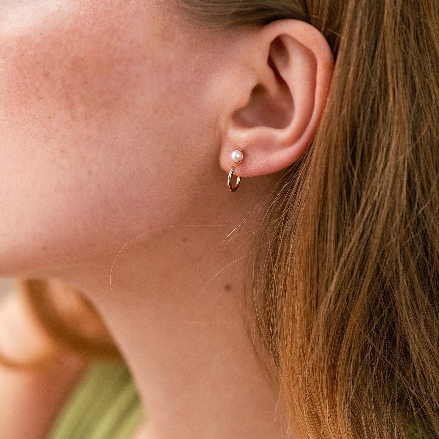 Close-up of an ear wearing a gold hoop earring with a pearl stud-everyday gold earrings