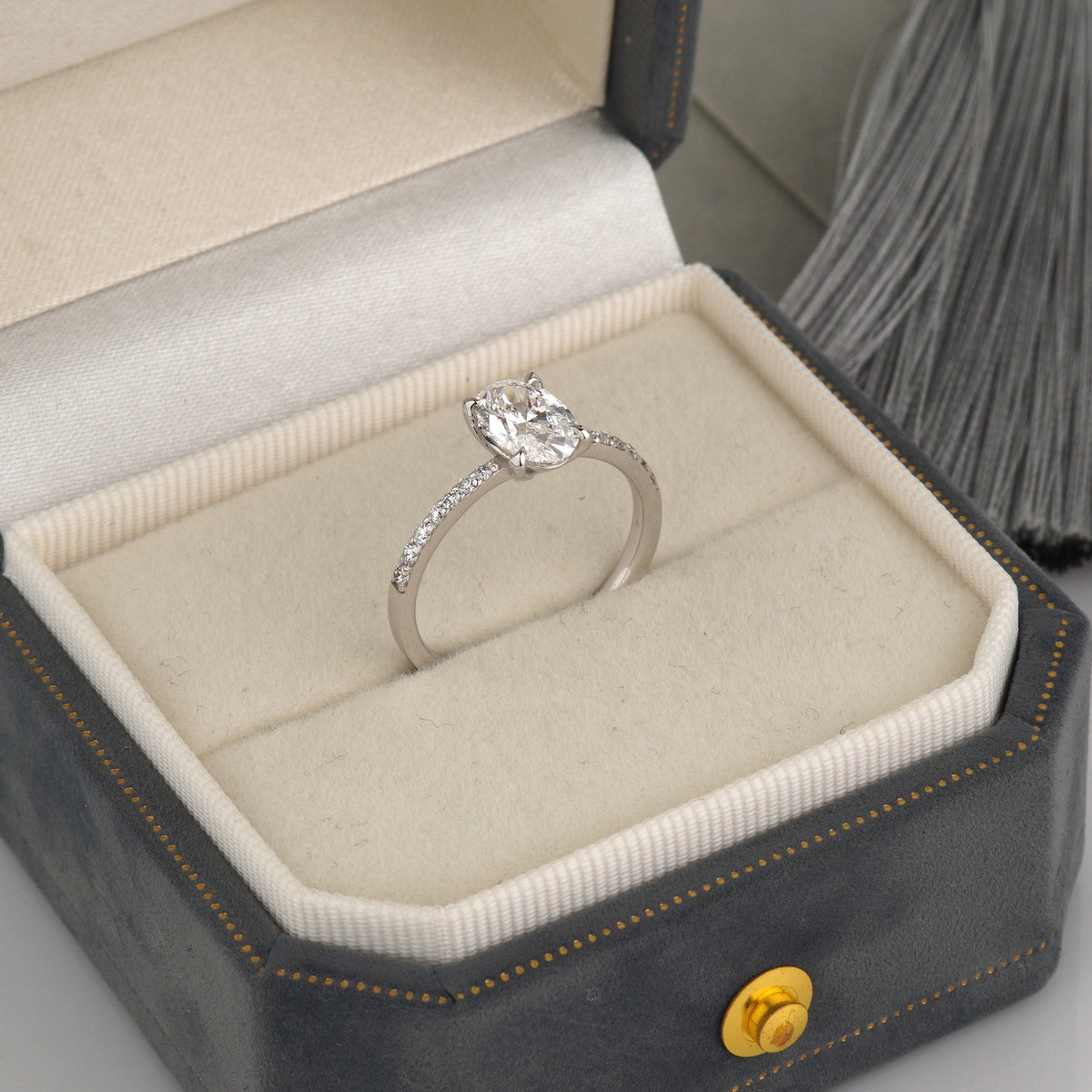A silver engagement ring with a round-cut center stone and small side stones, displayed in an open dark gray ring box with a cream velvet interior-lab diamond ring-oval engagement ring-solitaire diamond ring