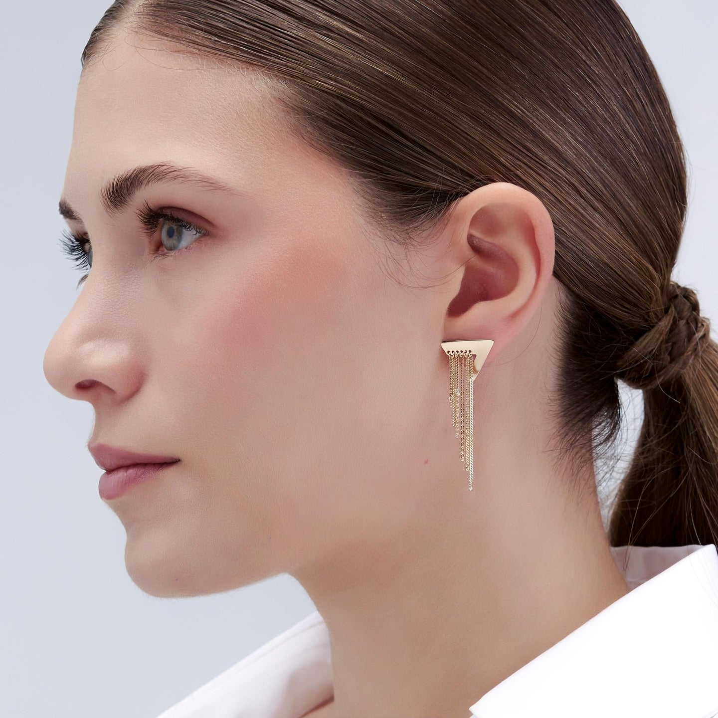 Woman wearing Solid Gold Fringe Earrings- geometric triangle stud accented by delicate, cascading gold chains