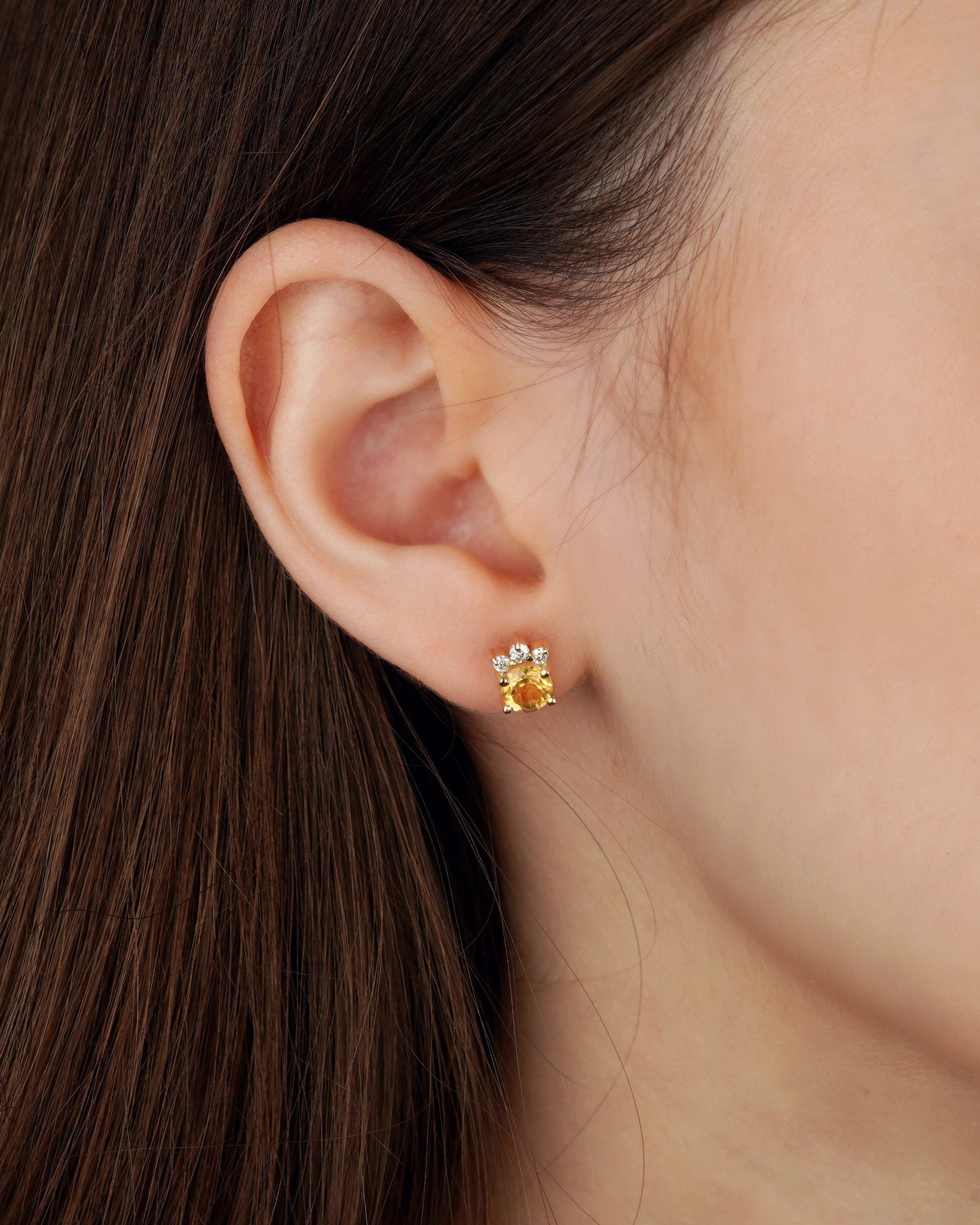 A close-up of a person's ear wearing a small gold stud earring with a floral design and tiny clear stones-Stones: Citrine + Moissanites (0.15 ct)-Closure: stud (screw-back)-Weight: 2.3–2.5 g