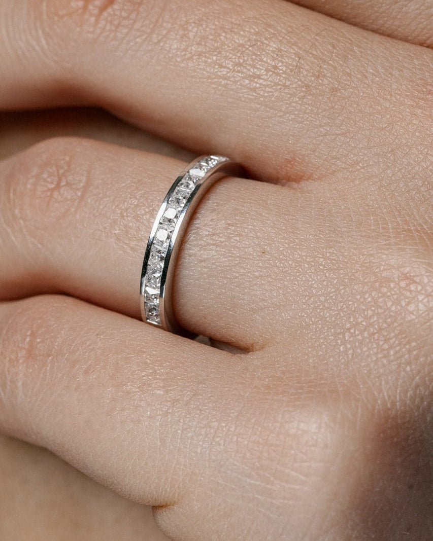 A close-up of a silver eternity band ring with small clear stones set along the band, worn on a finger-Free engraving on rings and comfort-fit lens option available upon request