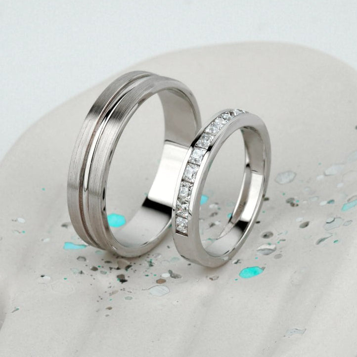 Two polished silver rings displayed on a white sculptural hand-shaped stand. One ring is smooth and matte, while the other is engraved with a row of clear stones-Metal: 14k Gold (585), solid — available in white, rose, or yellow