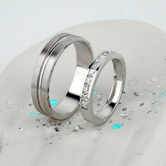 Two polished silver rings displayed on a white sculptural hand-shaped stand. One ring is smooth and matte, while the other is engraved with a row of clear stones-Metal: 14k Gold (585), solid — available in white, rose, or yellow