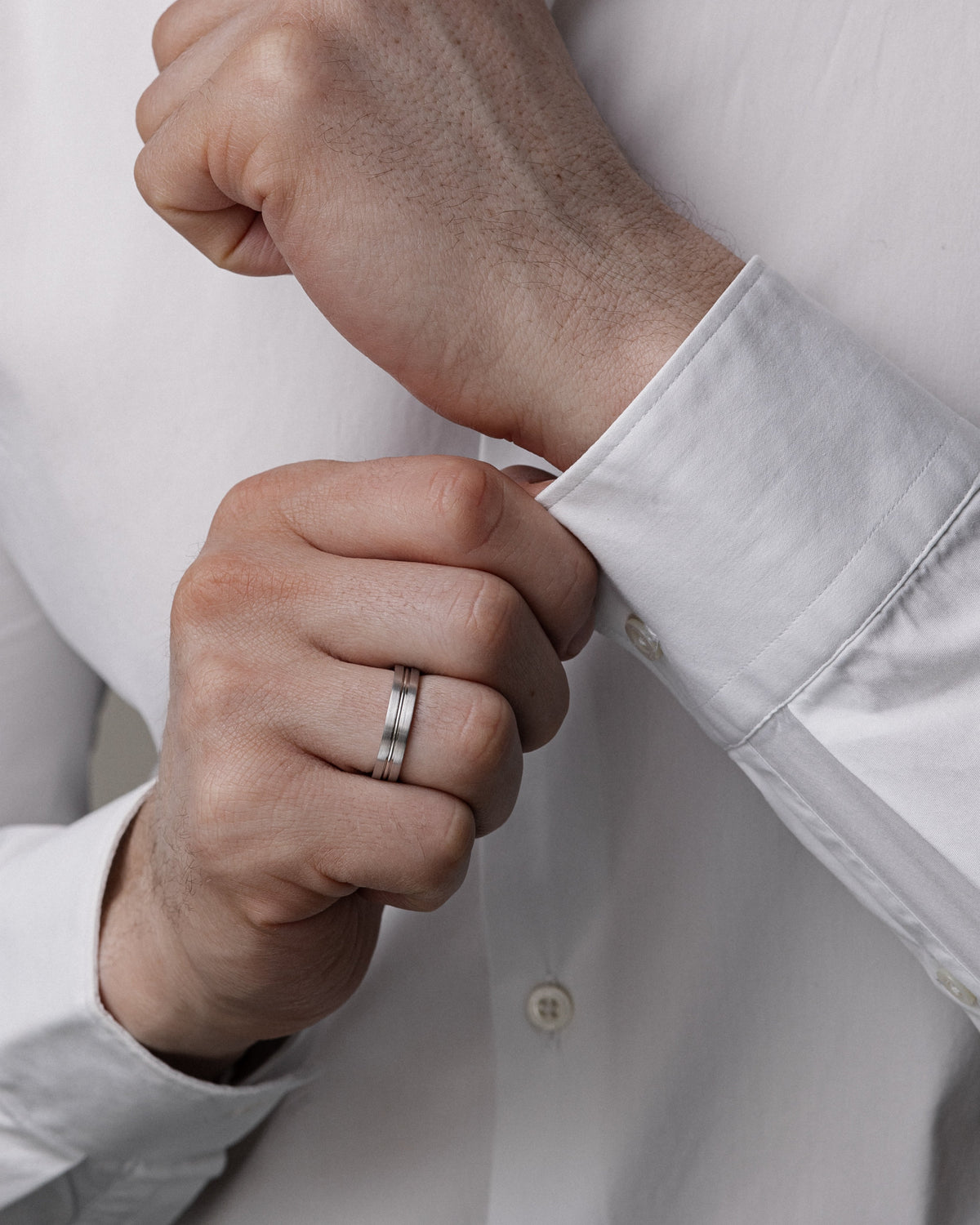A close-up of a man's hands adjusting the cuff of a white dress shirt, wearing a slim silver band ring on his finger-Men's band: 5 mm wide, brushed finish with polished center groove