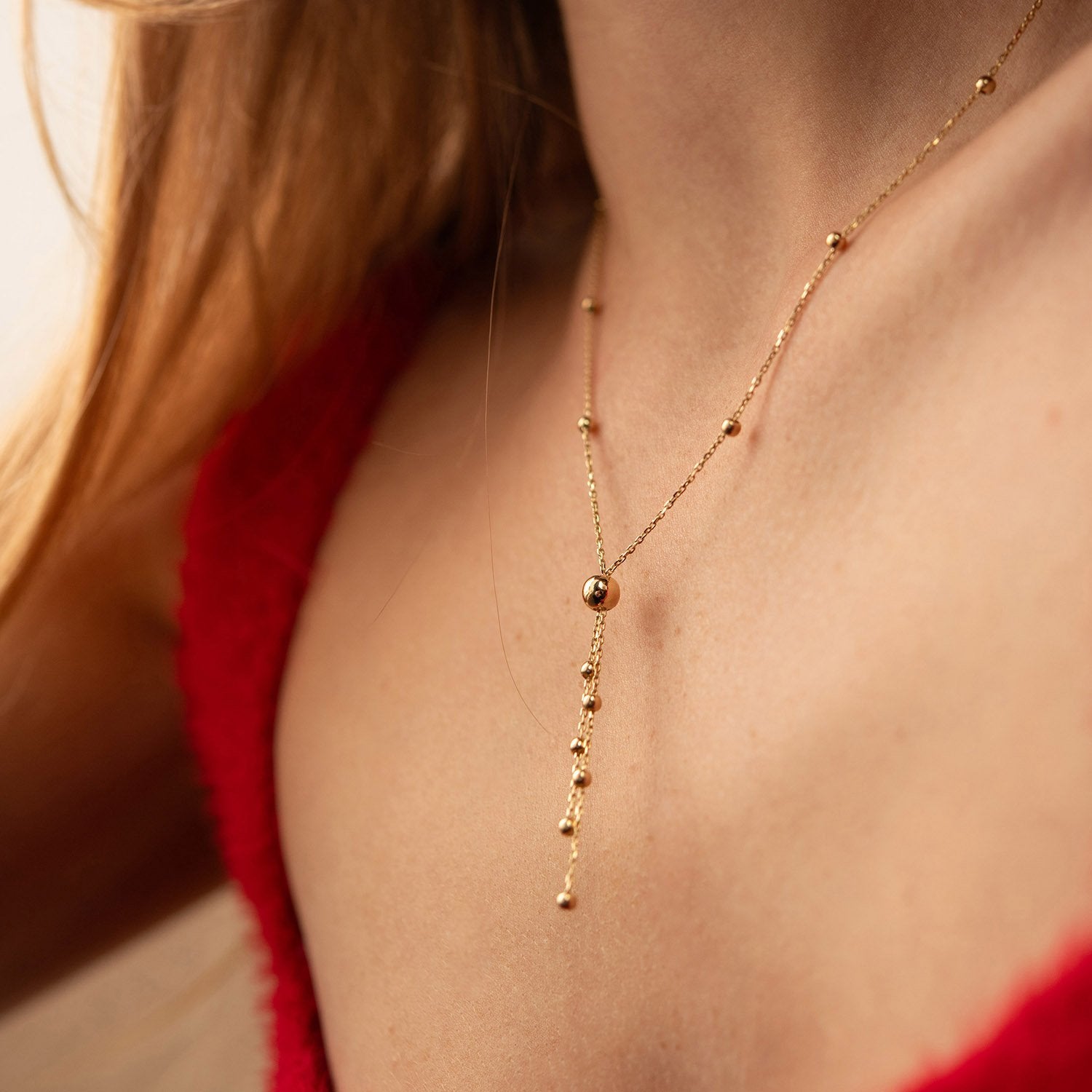 A close-up of a delicate gold Y-necklace with small bead accents worn by a model - weight 2.8 - 3 g 