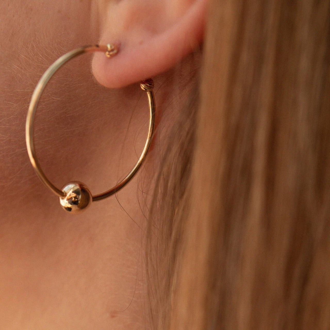 Gold hoop earring with a small ball detail worn by a person-28 mm gold hoop earrings with gold ball 