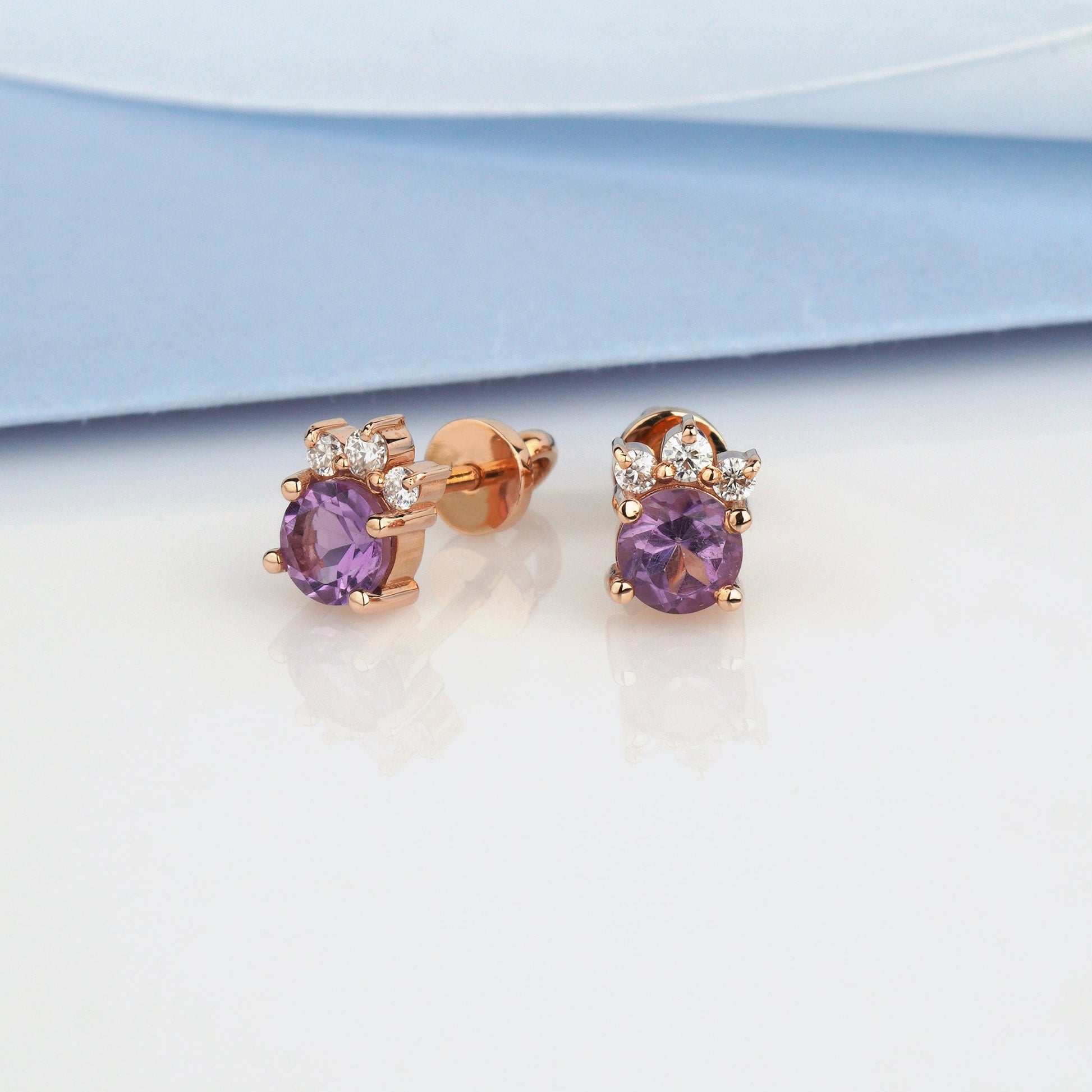 A pair of rose gold stud earrings with oval purple gemstones and small clear accent stones-gold flower earrings-diamond earrings-amethyst and moissanite earrings