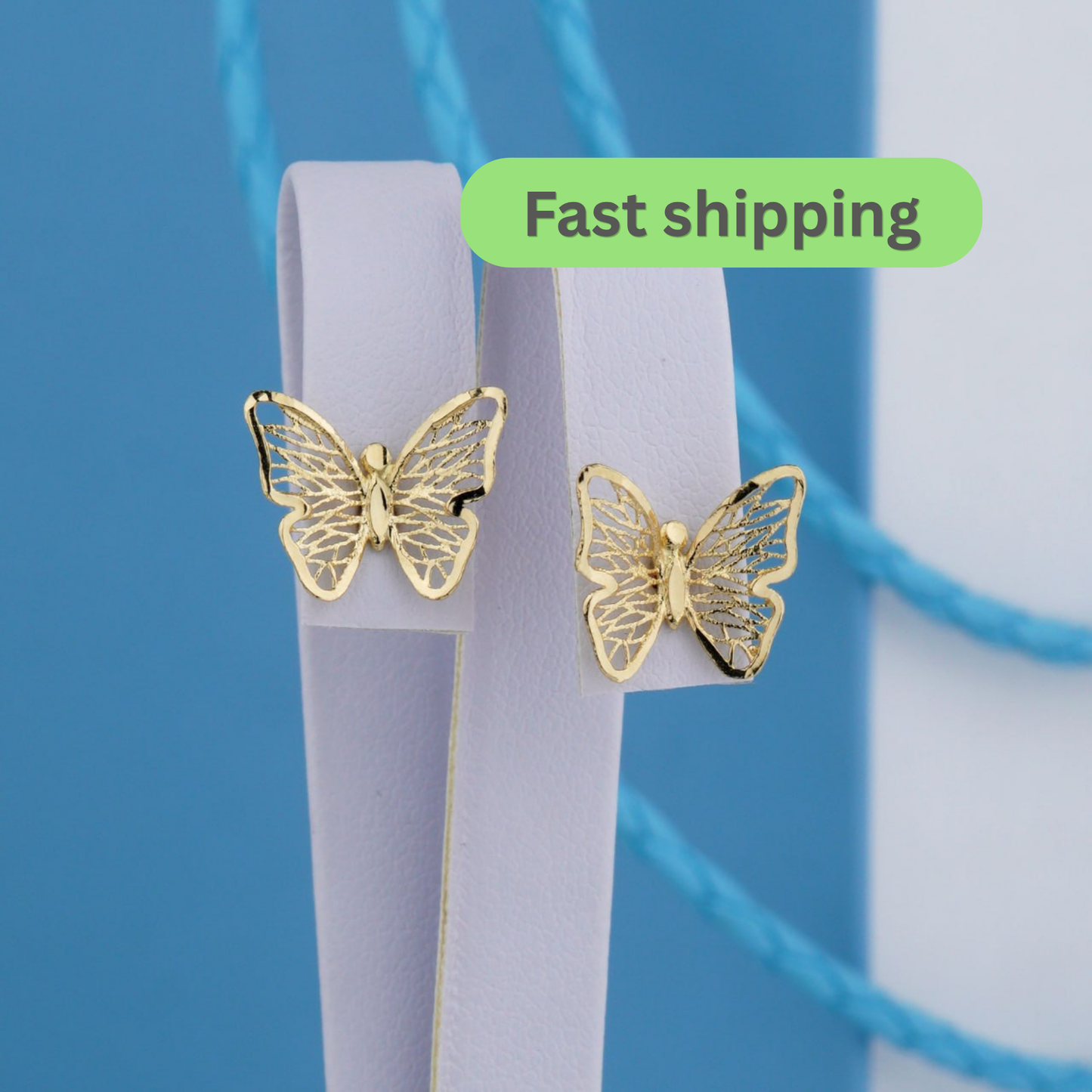 Two gold butterfly stud earrings displayed on a white jewelry stand against a blue background-gold butterfly earrings-14k gold studs-filigree earrings-butterfly stud earrings