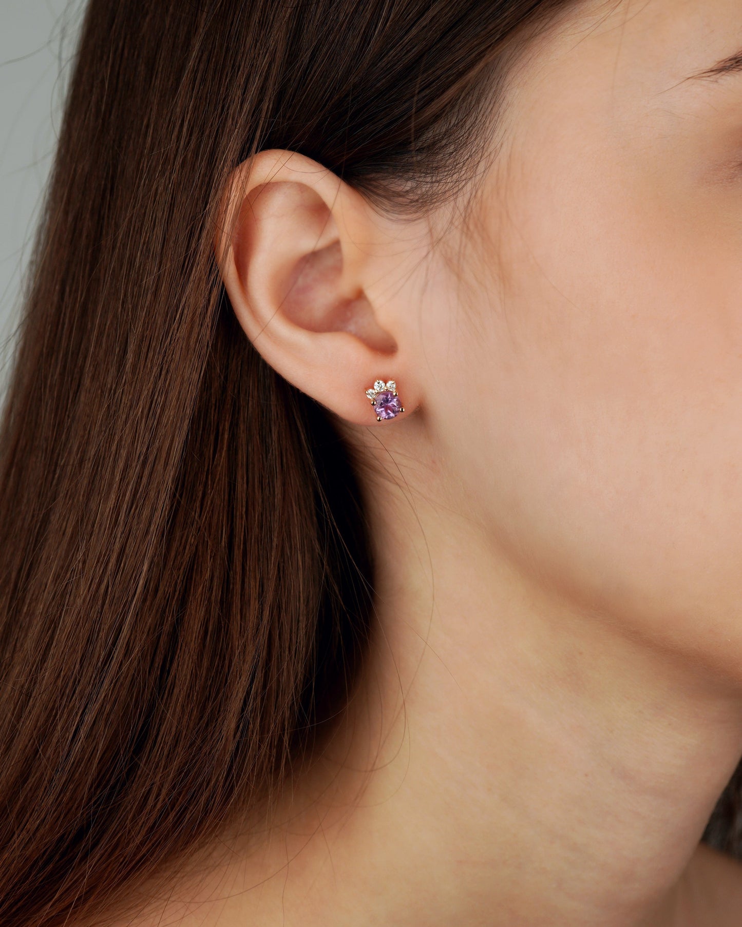 A close-up of a woman's ear wearing a small flower-shaped stud earring with a purple center and clear petals-Elegant Gold Flower Earrings with Gemstones
Gold Diamond Flower Stud Earrings