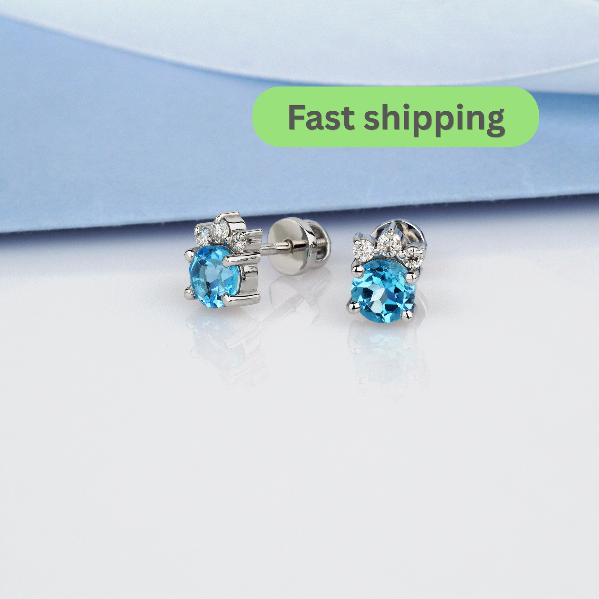 A pair of stud earrings with round light blue gemstones in silver settings, shown on a white surface -Elegant Gold Flower Earrings with Gemstones-Gold Diamond Flower Stud Earrings-Topaz Gold Earrings with Sparkling Moissanites