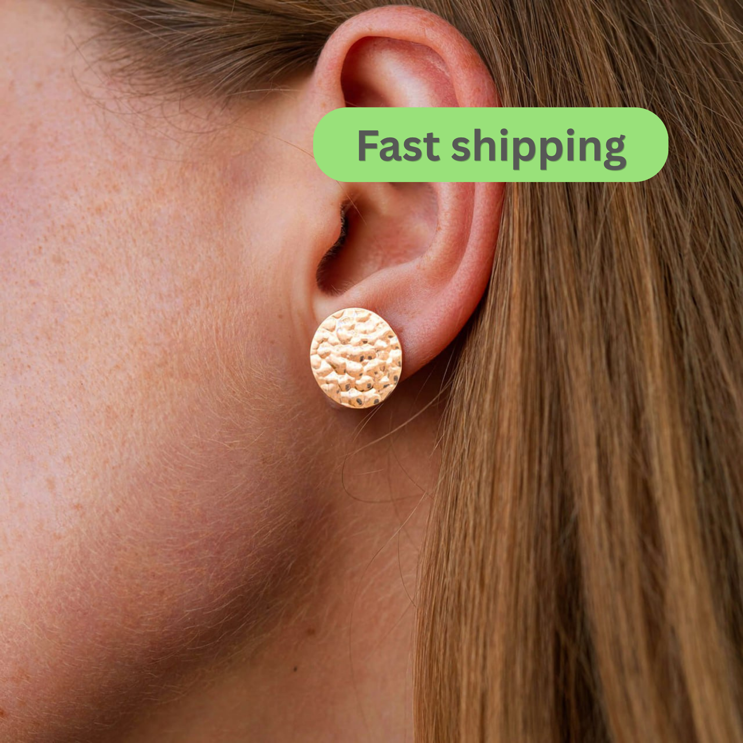 A close-up of a person's ear wearing a textured round stud earring in a warm metallic gold tone-gold disc earrings-hammered gold earrings-14k gold studs