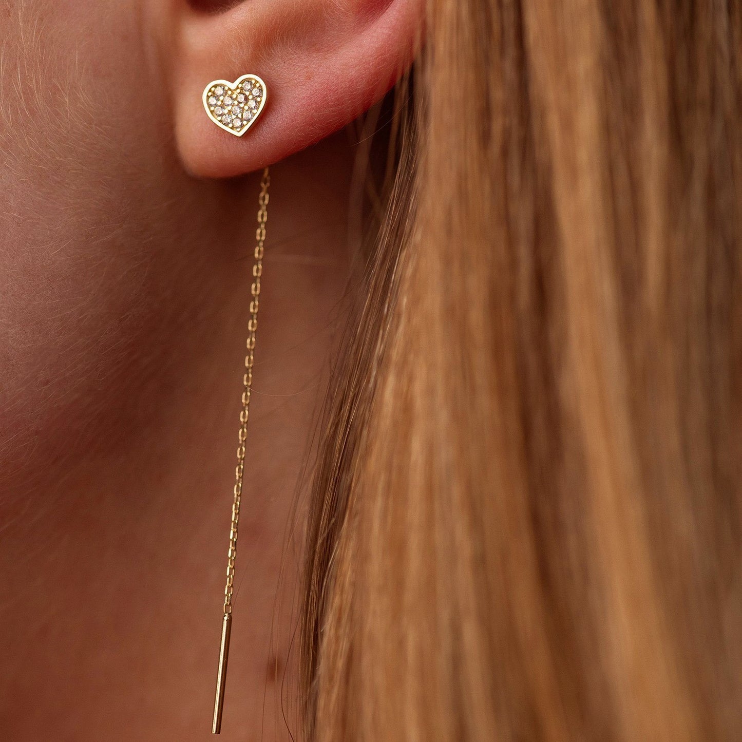 Gold heart-shaped earring with a dangling chain on an ear-Material: 14k solid gold, cubic zirconia stones