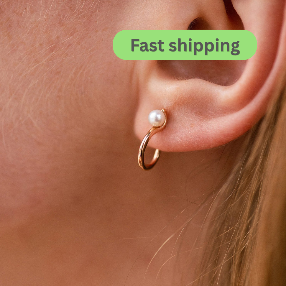 Gold hoop earring with a pearl accent worn by an ear