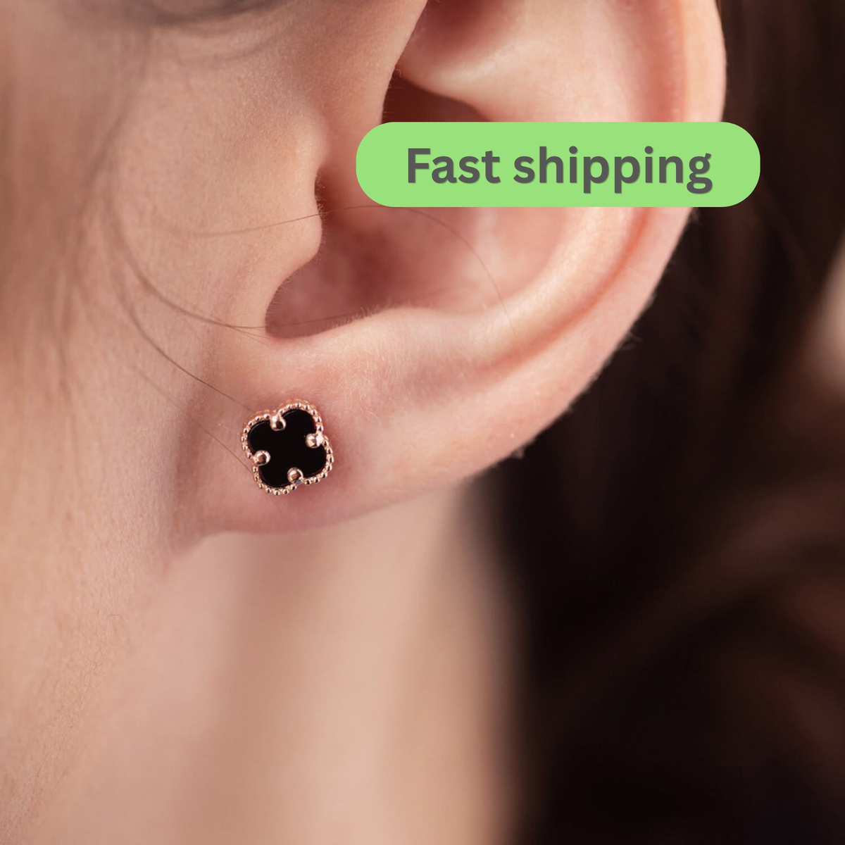 A close-up of a person's ear wearing a small black clover-shaped stud earring with a rose gold border-onyx earrings-clover stud earrings-rose gold earrings-14k gold studs