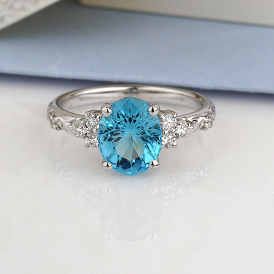 A silver ring featuring a round-cut light blue gemstone in the center, flanked by small clear stones on the shoulders-Metal: 14k White Gold (585), solid