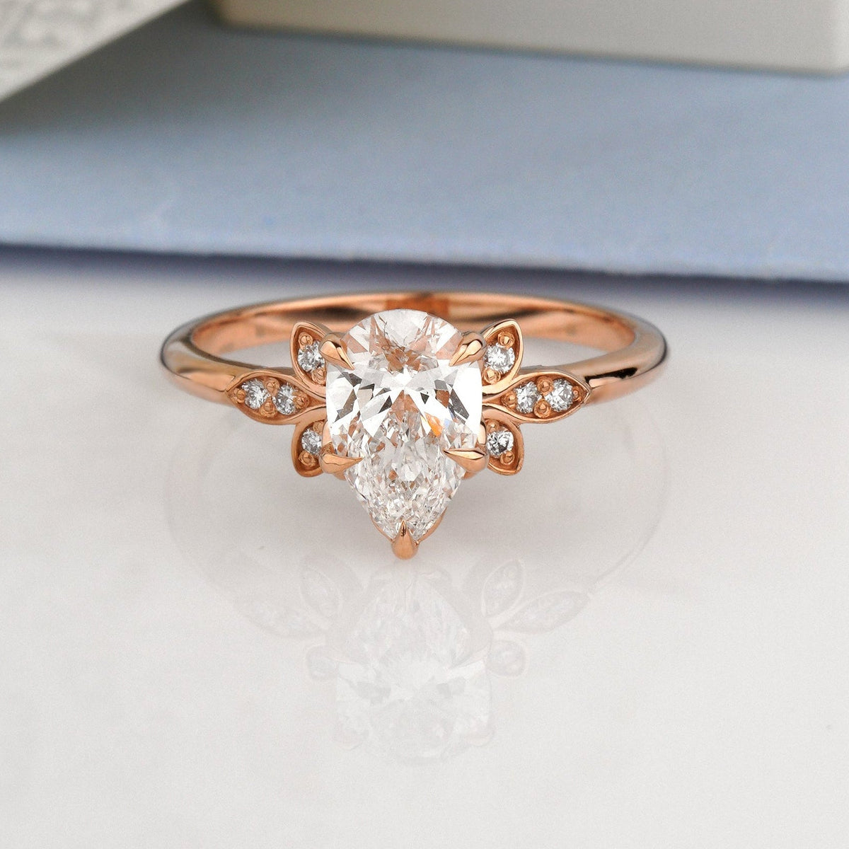 A rose gold ring with a pear-cut center stone and small side stones-Metal: 14k Rose Gold (585), solid-Center Stone: Lab-Grown Diamond, Pear Cut, 1.00 ct, IGI Certified
