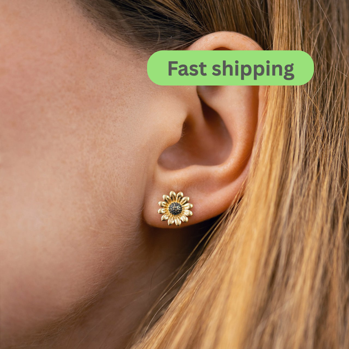 A close-up of a person's ear wearing a small gold flower-shaped stud earring with a dark center-sunflower earrings-gold stud earrings-14k gold studs