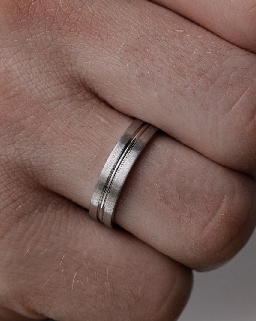 A close-up of a silver band ring with two parallel grooved channels, worn on a person's finger-Men's band: 5 mm wide, brushed finish with polished center groove