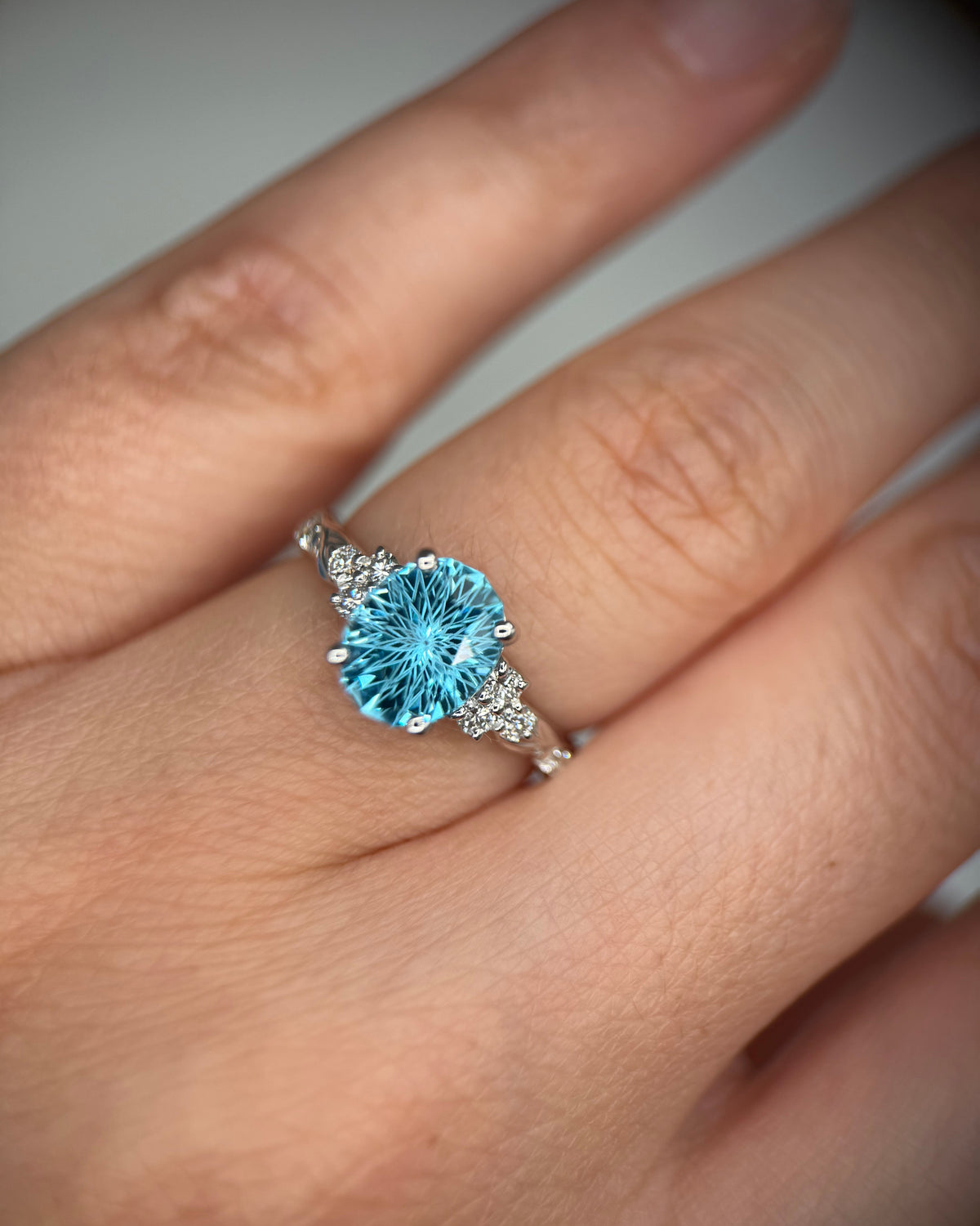 A close-up of a hand wearing a silver ring with a large round-cut light blue gemstone and small accent stones on the band-topaz gold ring-unique engagement ring-statement gemstone ring