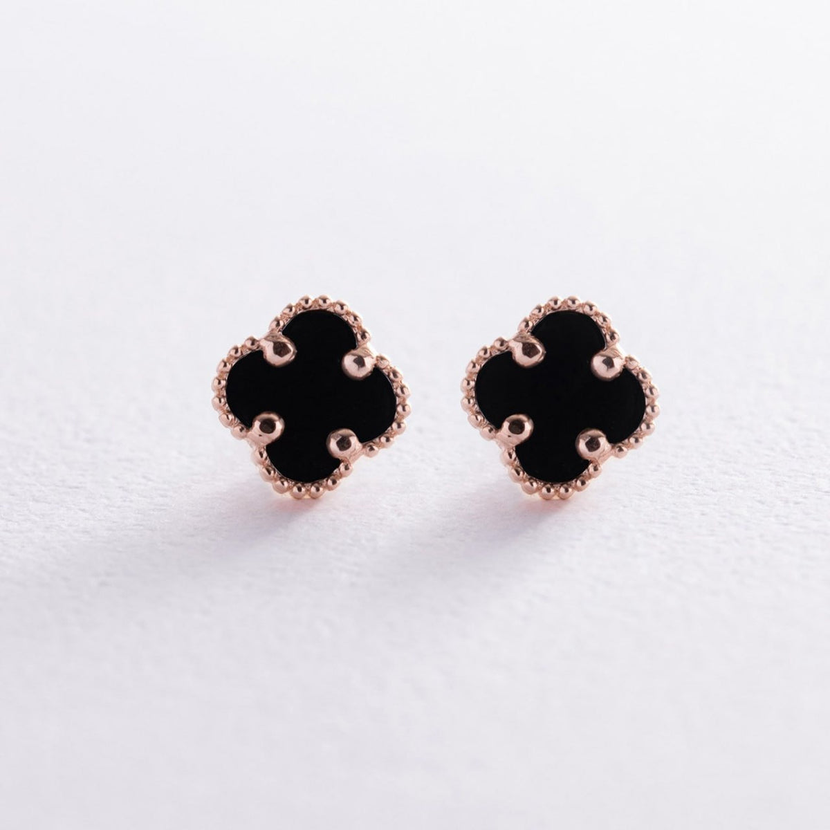 A pair of black clover-shaped stud earrings with rose gold beaded borders, displayed on a clean white surface-black onyx jewelry-minimalist gold earrings-solid gold earrings