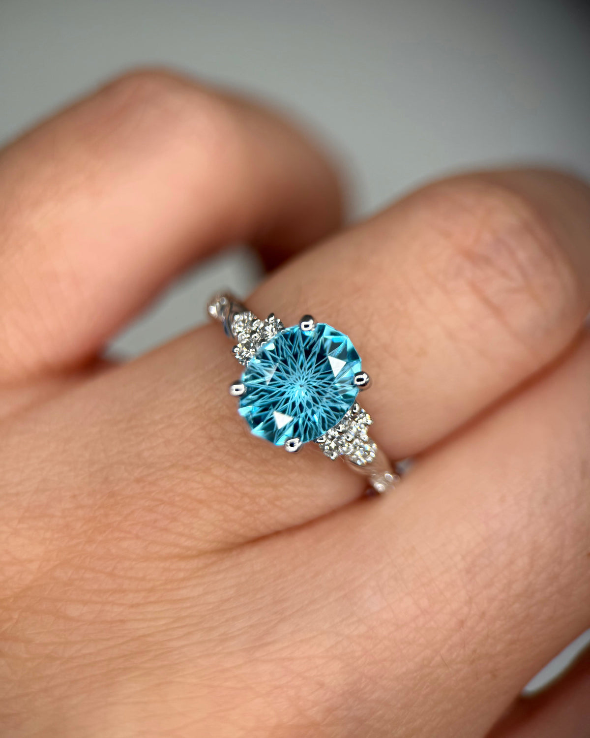 A close-up of a hand wearing a silver ring with a large round-cut light blue gemstone and small clear accent stones on the shoulders-Center Stone: Natural Swiss Blue Topaz, Oval Cut, 1.5 ct-Accent Stones: Lab-Grown Diamonds, 0.21 ct total