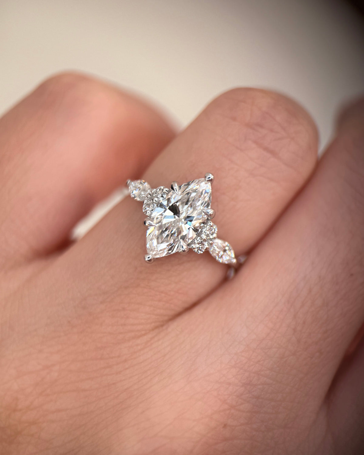 A close-up of a ring worn on a finger, featuring a large princess-cut diamond center stone with marquise-cut side stones in a silver-toned setting-marquise engagement ring-cluster engagement ring-white gold engagement ring