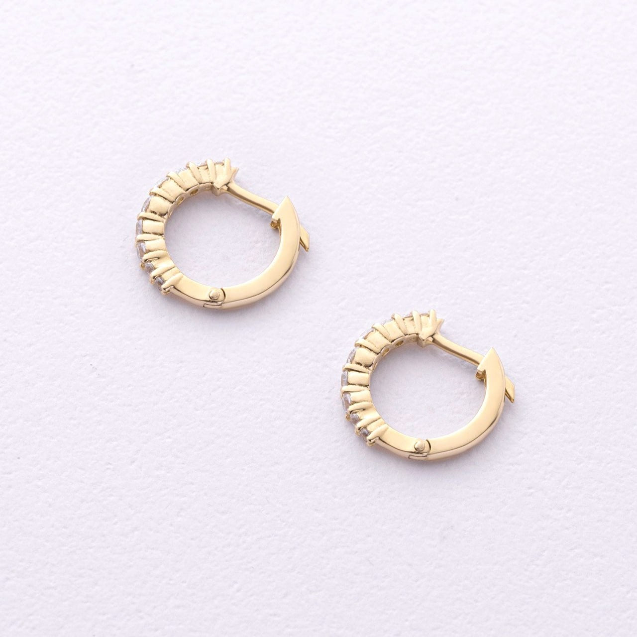 A pair of gold huggie hoop earrings with textured, beaded edges, displayed on a clean, light off-white textured background-14k gold hoops-cz hoop earrings-small huggie hoops