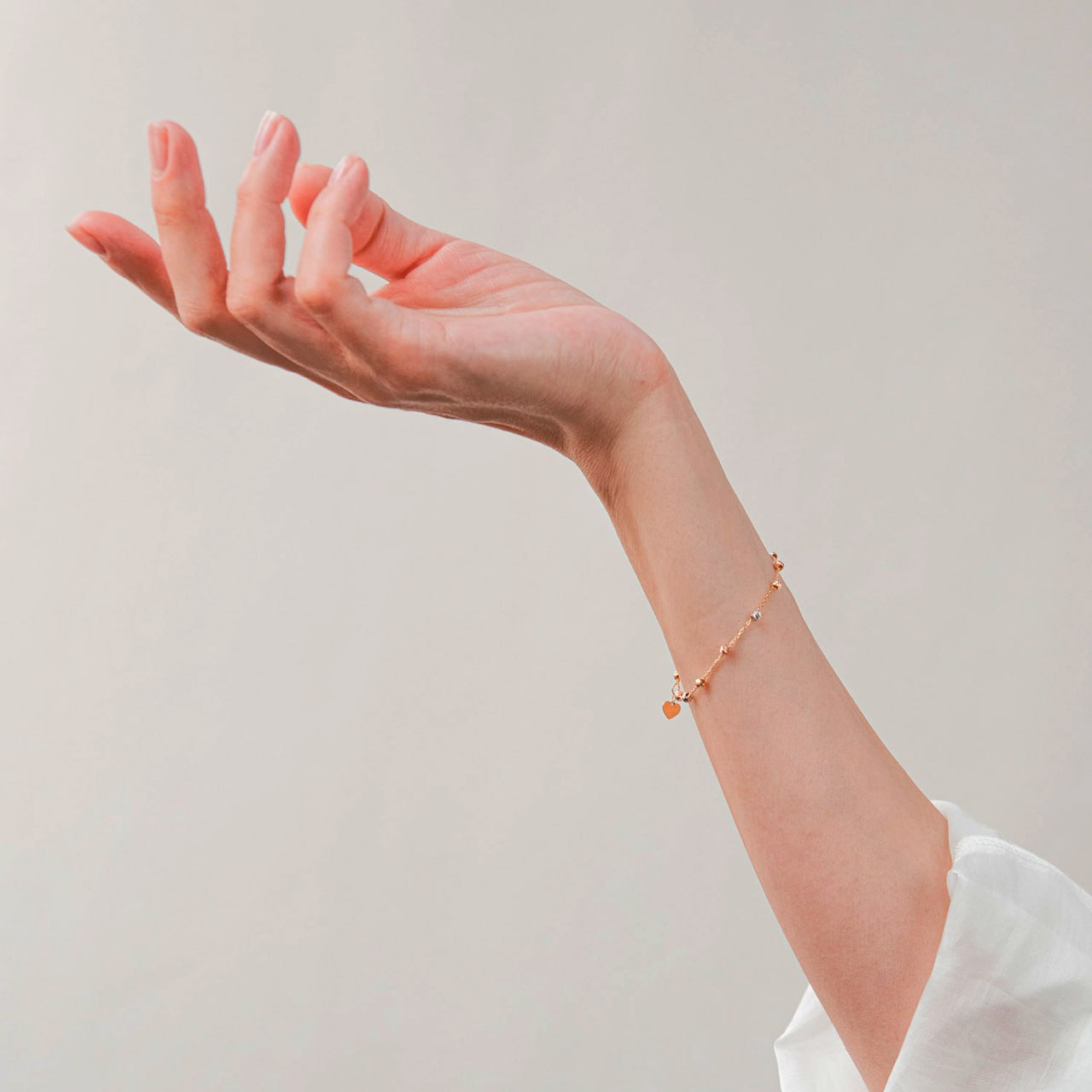 A delicate rose gold chain bracelet with tiny bead links and a small dangling charm, shown worn on a person's wrist -stackable gold bracelet-everyday gold bracelet gift