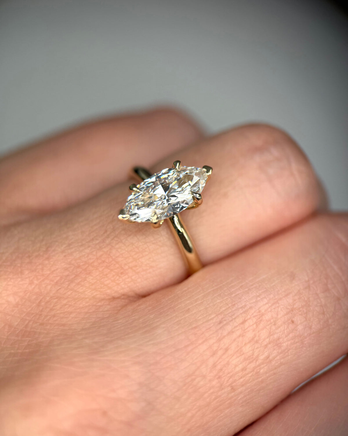 A close-up of a hand wearing a yellow gold ring with a marquise-cut clear gemstone in a prong setting-14k gold engagement ring-marquise engagement ring-igi certified diamond
