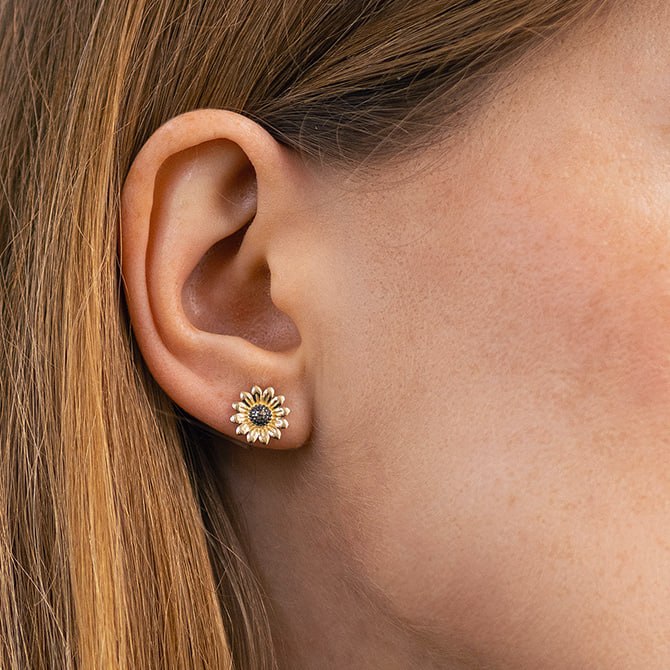 A close-up of a person's ear wearing a small gold daisy stud earring with a dark blue center-flower stud earrings
flower gold earrings-minimalist gold earrings