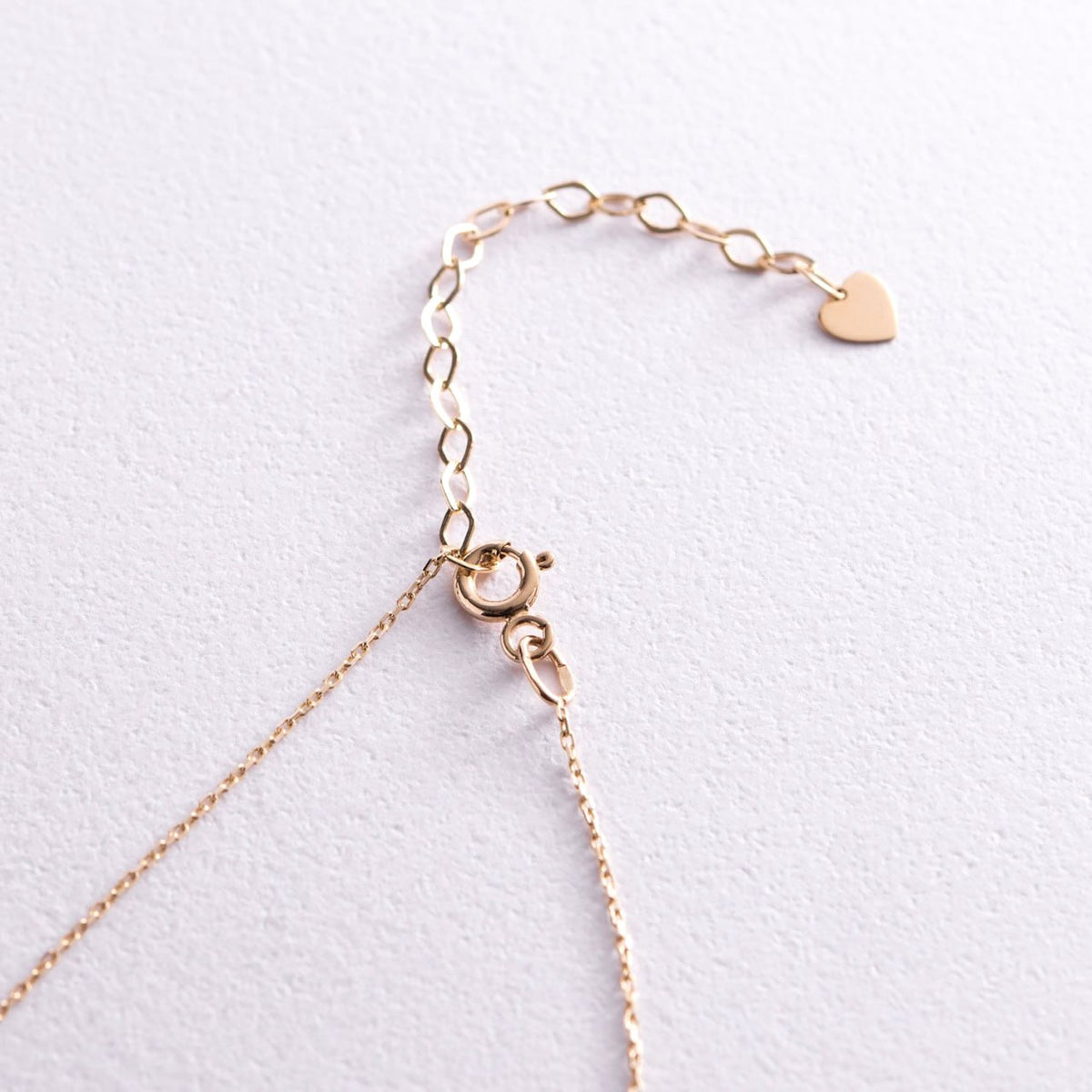 A close-up of a delicate rose gold chain necklace showing the clasp, extender links, and a small heart-shaped charm-14k yellow gold, this necklace is effortlessly elegant — perfect for layering or wearing alone.-Clasp: Lobster clasp