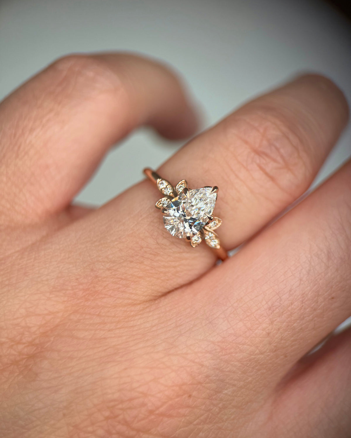 A close-up of a hand wearing a rose gold ring with a marquise-cut center stone and smaller diamond accents-floral halo engagement ring
romantic diamond ring
lab diamond engagement ring