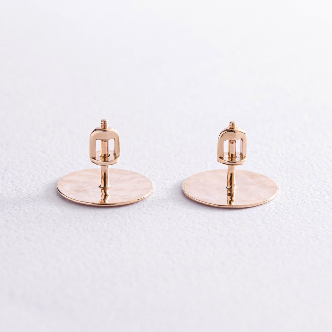 A pair of rose gold disc stud earrings with a geometric cage post, displayed on a textured light gray background-solid gold earrings-statement stud earrings-circle earrings