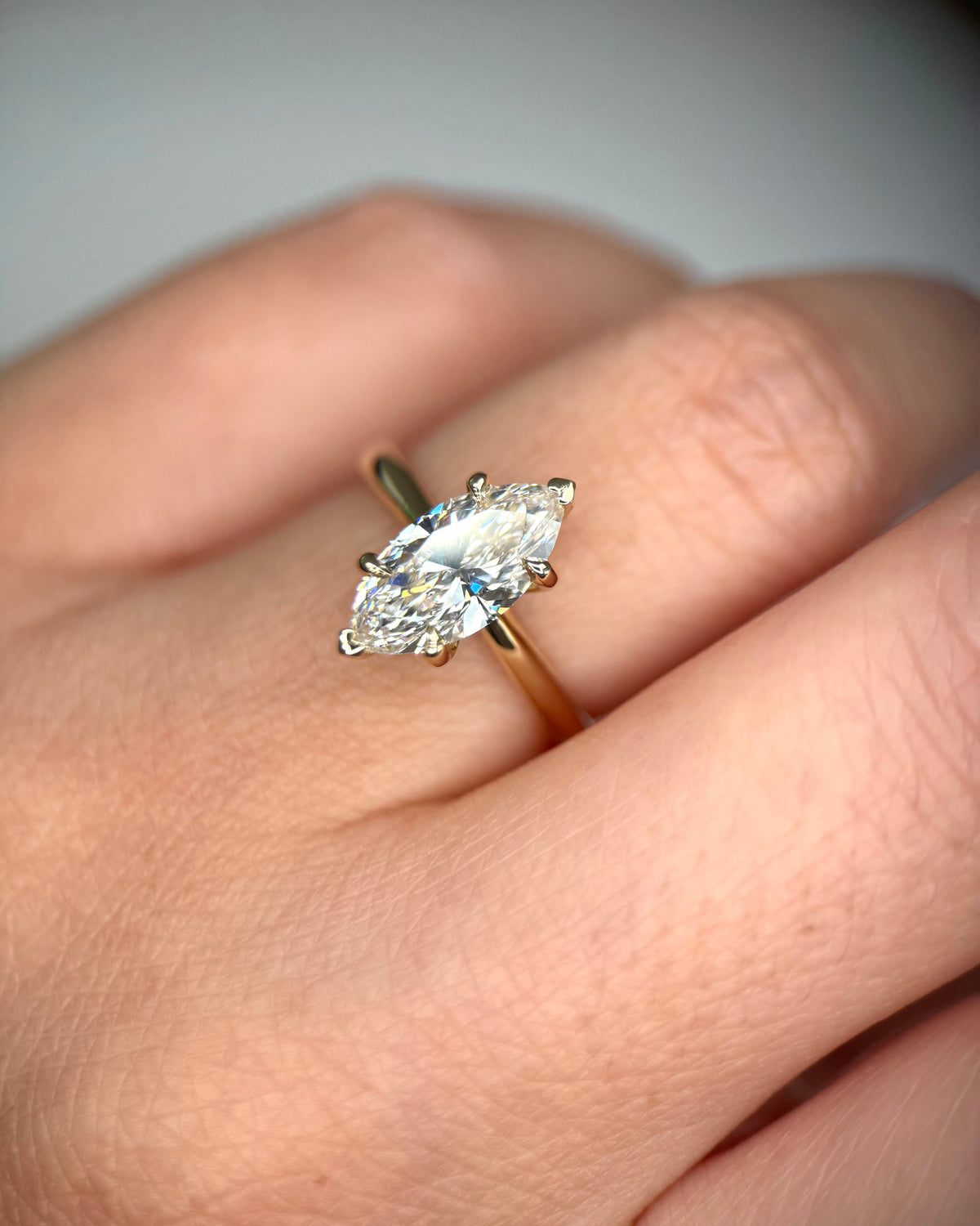 A close-up of a hand wearing a yellow gold ring with a marquise-cut clear gemstone in a prong setting-elongated diamond ring-unique engagement ring-1.5 ct marquise diamond engagement ring