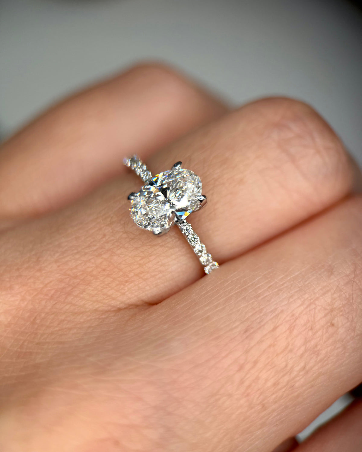 A close-up of a diamond engagement ring with a three-stone center and a pavé band, worn on a person's finger-classic engagement ring
white gold engagement ring
1 ct oval diamond ring