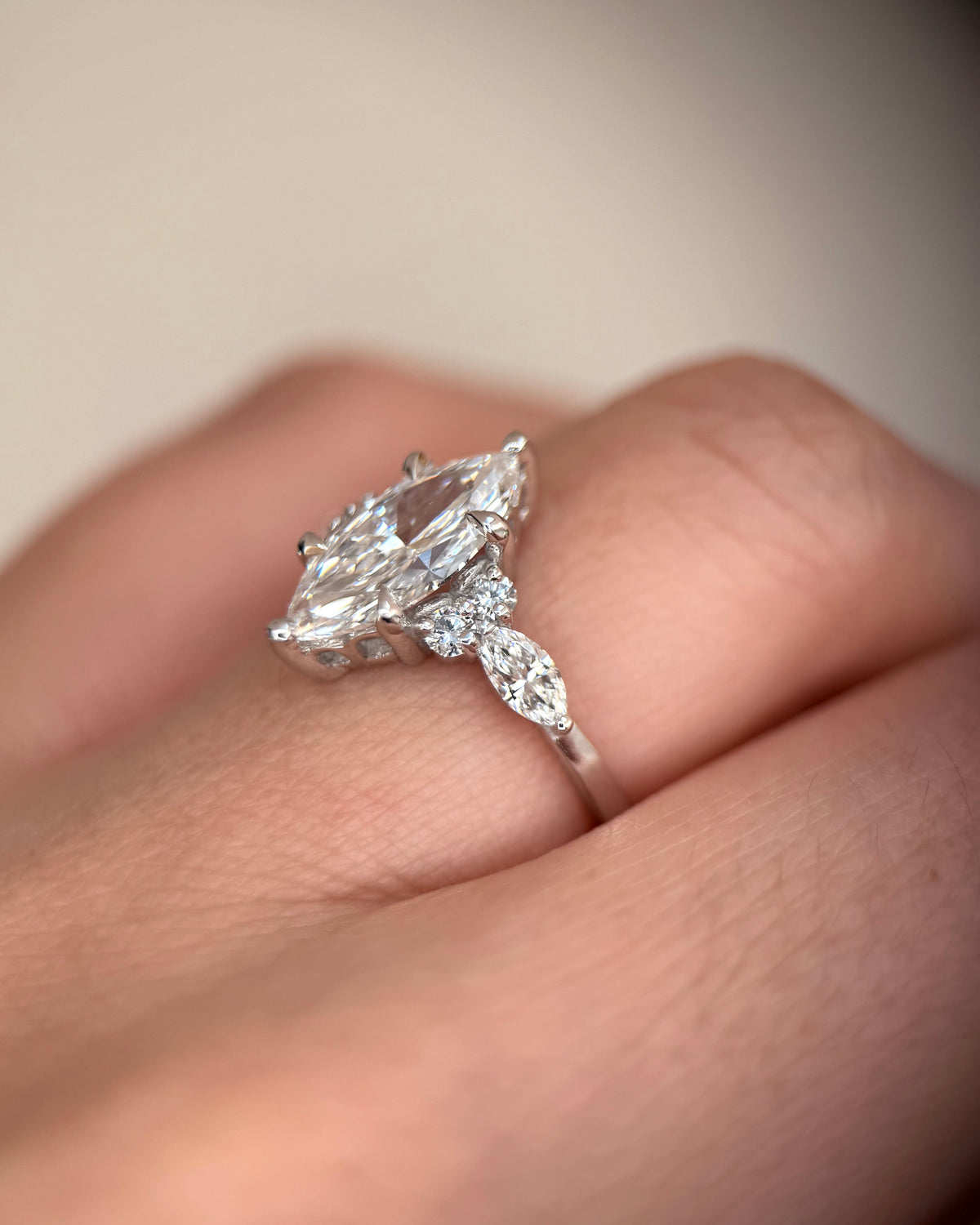 A close-up shot of a silver-toned ring with a marquise-cut center stone and smaller marquise side stones, worn on a person's finger -art deco engagement ring-lab diamond ring-unique engagement ring