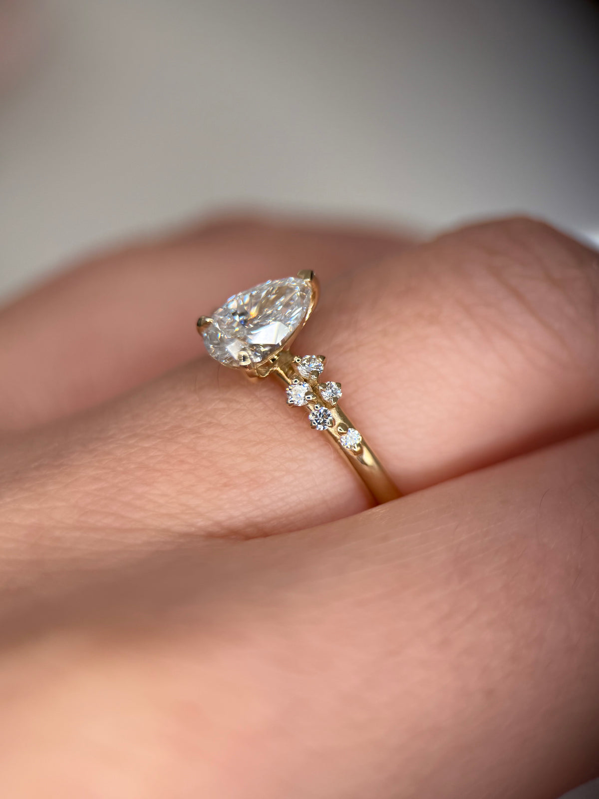 A close-up of a yellow gold ring with a marquise-cut clear gemstone and small accent stones on the band, worn on a person's finger-unique engagement ring-vintage inspired ring-gold engagement ring