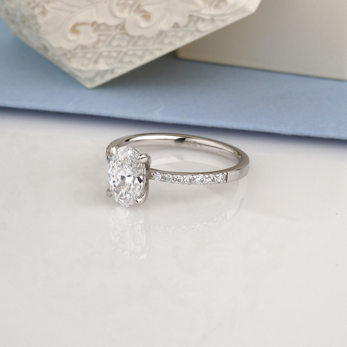 An oval-cut diamond engagement ring in a silver-colored setting with a pavé band-Center Stone: Lab-Grown Diamond, Oval Cut, 1.00 ct, IGI Certified
