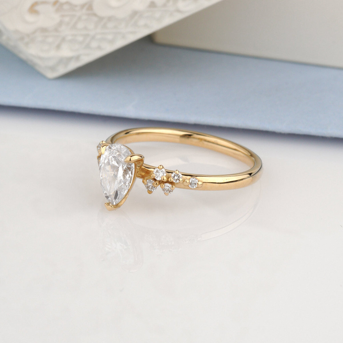 A gold ring with a pear-cut clear gemstone and small accent stones-cluster engagement ring-igi diamond ring-pear shaped ring