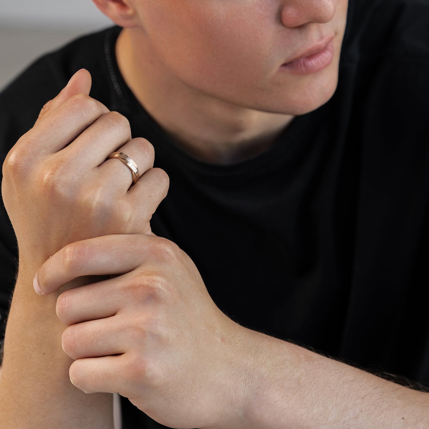 A close-up shot of a young man with short brown hair wearing a simple gold band ring on his ring finger-unique wedding ring -matte wedding band 
