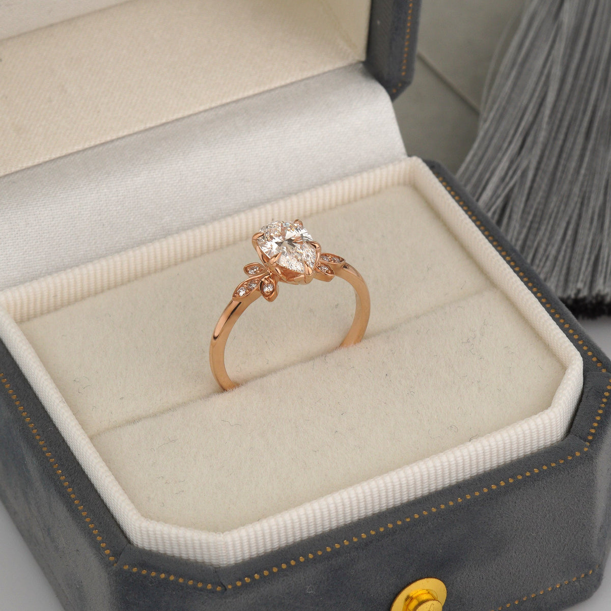 A rose gold ring with a heart-shaped clear gemstone is displayed inside an open dark gray velvet jewelry box with a cream-colored lining-Center Stone: Lab-Grown Diamond, Pear Cut, 1.00 ct, IGI Certified